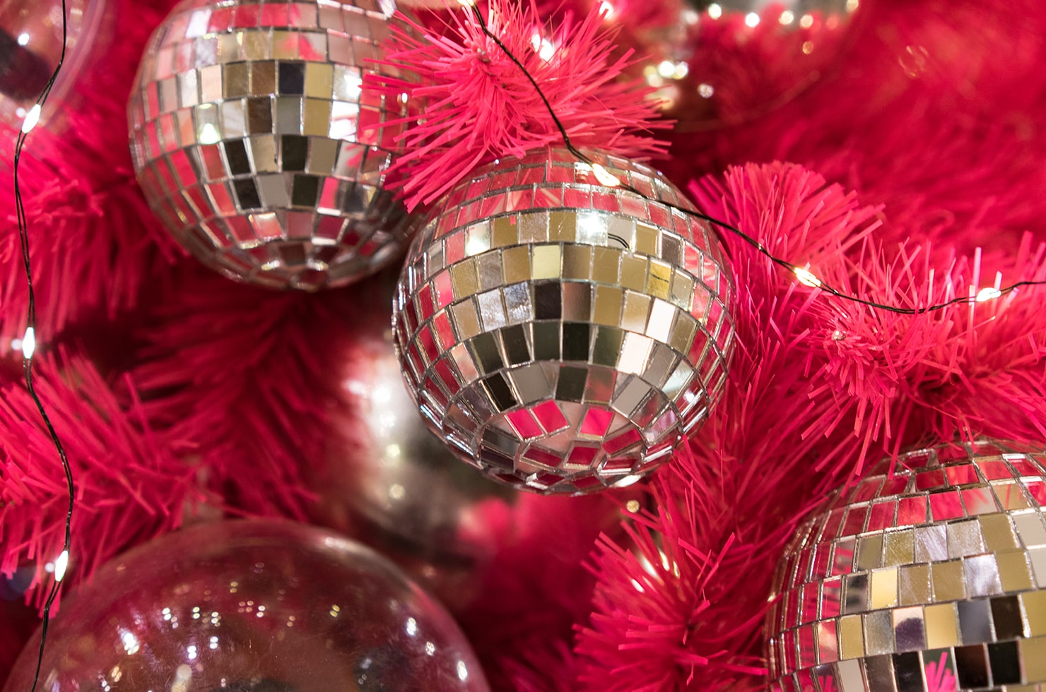 An un-close shot of a red Christmas tree decorated with silver disco baubles and LED lights.