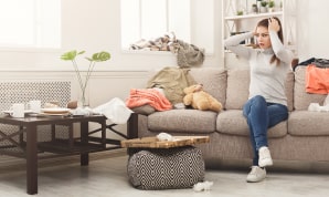 Desperate woman sitting on the sofa in a cluttered living room.