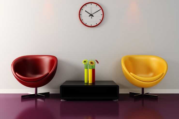 A room with red and yellow chairs, a red and yellow vase and a wall clock