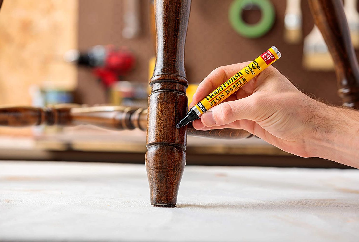 A hand holding a stain marker and painting over a scratch on a wooden furniture piece.