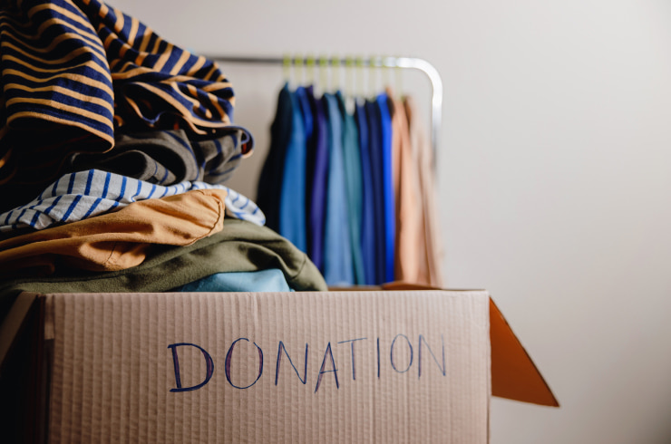 A cardboard donation box filled with clothes and a clothes rack in the background.