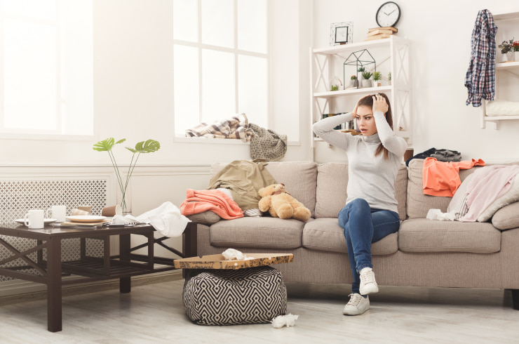 Desperate woman sitting on the sofa in a cluttered living room.