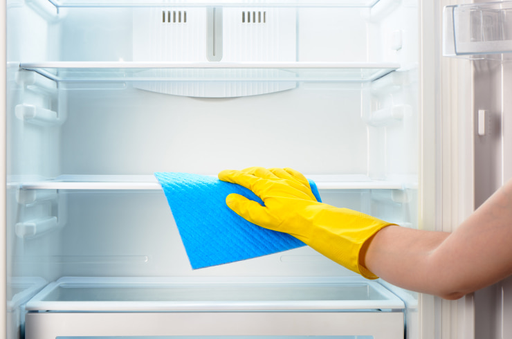 A woman in yellow gloves cleaning the fridge.