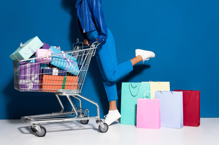 A woman with a shopping cart, lots of bags and gift boxes on a blue background.